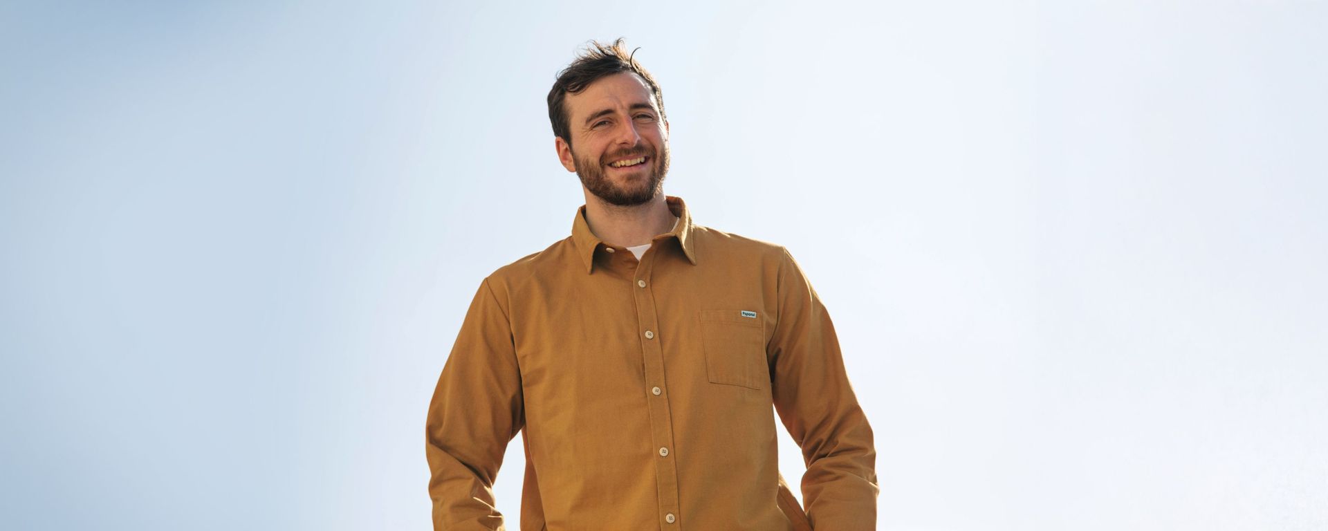Man wearing a brown shirt under a clear sky, representing men's sustainable clothing.