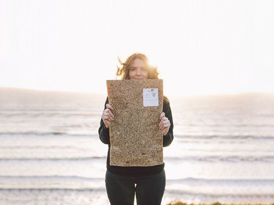 Woman standing in front of a seaside sunset holding Teemill's marine print paper packaging.